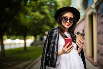 Young asian woman with hat and sunglasses reading using phone in the street. Female asian woman...