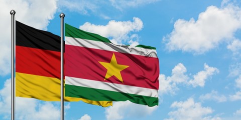 Germany and Suriname flag waving in the wind against white cloudy blue sky together. Diplomacy concept, international relations.