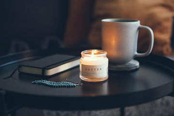 Cozy interior ditails. Little round table with cup of delicious tea and candle, notepad and...