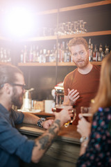 Cheerful friends leaning on bar counter, drinking beer and chatting with bartender. Night out.