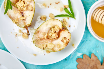 Tasty roast pears with honey and walnuts on white plates on blue background table.