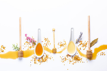 white spoons and honey sticks, with spilled honey, .bee pollen and flowers isolated on white...
