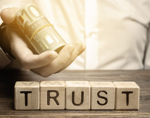 Wooden blocks with the word Trust and money in the hands of a businessman. Trust relationships...