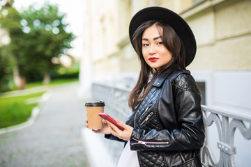 Fototapeta premium Young asian woman reading using phone reading news or texting sms on smartphone while drinking coffee on break from work.