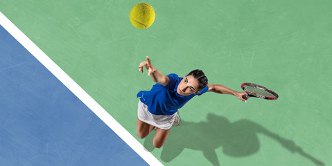Young caucasian brunette woman in blue shirt playing tennis at the court. Hits ball with racket,...