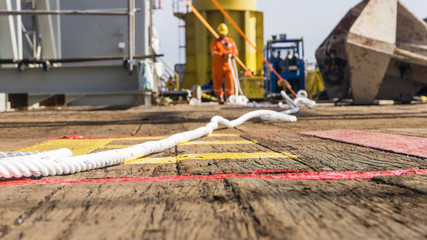 Offshore rigger or roughneck preparing rigging for tugger rope on deck of a construction barge at oil field