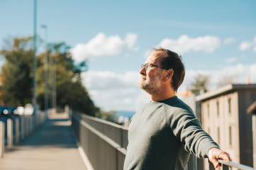 Outdoor portrait of 50 - 55 year old man wearing green pullover and eyeglasses