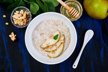 A bowl of porridge with pears slices and walnuts  on dark blue background.