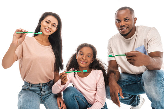 happy african american parents with daughter holding toothbrushes and smiling at camera isolated on white