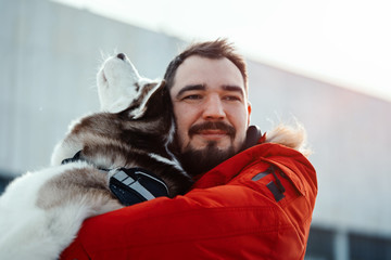 Man hugging Siberian Husky dog on a walk in modern park on sunny winter day. Pure love and friendship