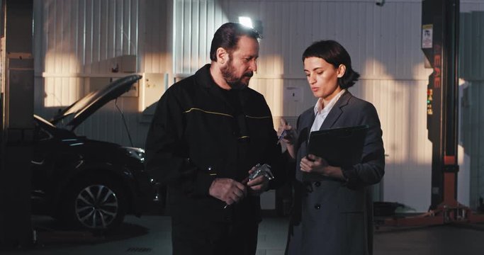 Office manager woman in a suit have a conversation with a service auto worker in the garage they analyzing the plan of work