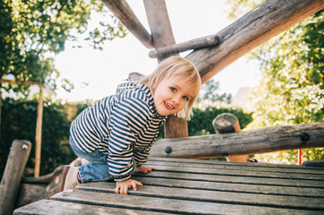 Outdoor portrait of happy toddler girl playing on playground, active child having fun in kids park