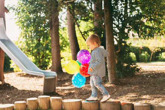 Funny kid girl playing with colorful balloons on playground