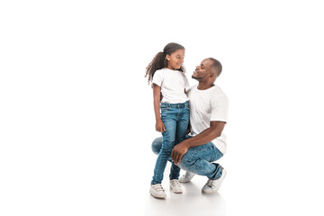 happy african american father squatting and talking to adorable daughter on white background