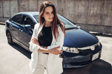 Fashion Stylish Girl in White Suit Posing Near the Blue Car and Holds Keys in Hand