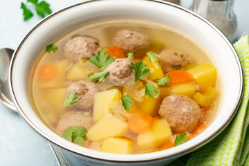 Soup with meatballs and vegetables in bowl on concrete background. Selective focus.