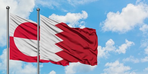 Greenland and Bahrain flag waving in the wind against white cloudy blue sky together. Diplomacy...