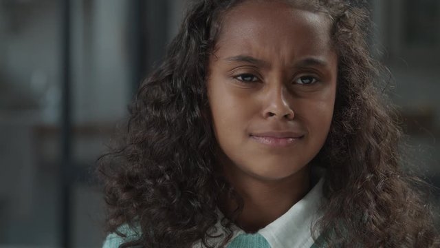 Portrait of cute african american elementary age girl with curly hair expressing disappointment, feeling resentment and sadness, looking with eyes full of tears, hopelessness , depressed and unhappy.