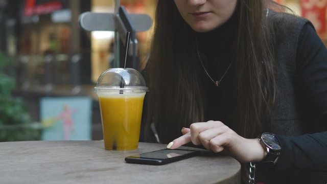 Young woman browsing on smartphone in cafe on wooden table, drinking juce. Businesswoman typing on mobile phone. 4K UHD
