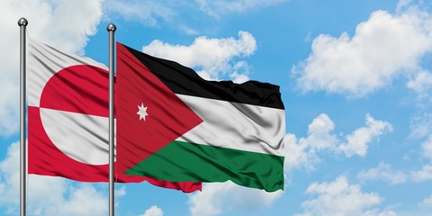 Greenland and Jordan flag waving in the wind against white cloudy blue sky together. Diplomacy...