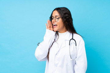 Young doctor woman over isolated blue background shouting with mouth wide open