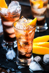 Alcoholic cocktail with mango, cranberries, lime, crushed ice and liquor, dark wooden bar counter background, selective focus