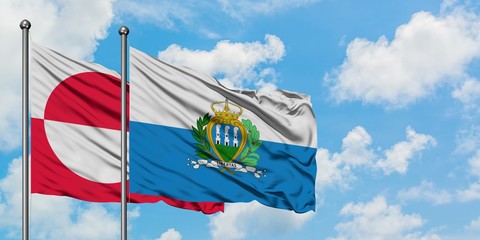 Greenland and San Marino flag waving in the wind against white cloudy blue sky together. Diplomacy concept, international relations.