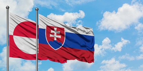 Greenland and Slovakia flag waving in the wind against white cloudy blue sky together. Diplomacy...