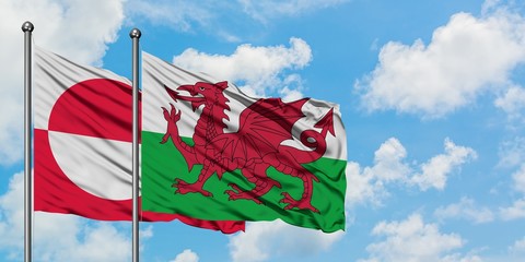 Greenland and Wales flag waving in the wind against white cloudy blue sky together. Diplomacy concept, international relations. © sezerozger