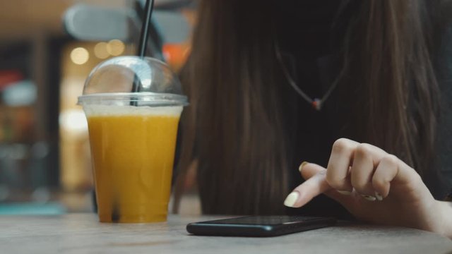 Young woman browsing on smartphone in cafe on wooden table, drinking juce. Businesswoman typing on mobile phone. 4K UHD