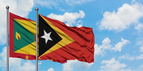 Grenada and East Timor flag waving in the wind against white cloudy blue sky together. Diplomacy...