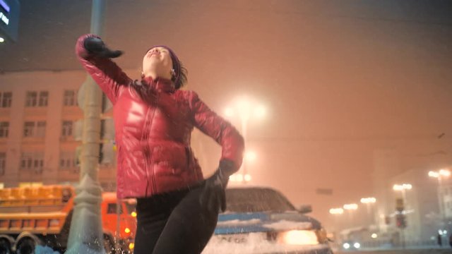 Happy young woman dancing energetic modern freestyle rap dance in city street during winter snowfall snowstorm. Slow motion, 4K UHD.