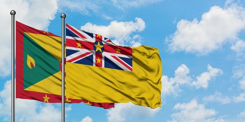 Grenada and Niue flag waving in the wind against white cloudy blue sky together. Diplomacy concept, international relations.