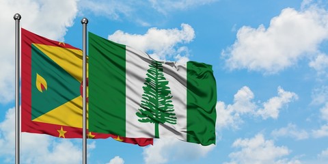 Grenada and Norfolk Island flag waving in the wind against white cloudy blue sky together....
