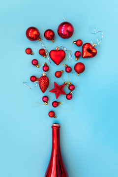 Red champagne bottle with red christmas ball, star and heart toys on blue background. Flat lay. Christmas greeting card. Christmas or New Year celebration concept. Copy space