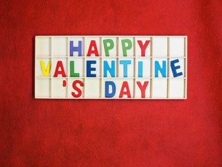 op view or directly above of multicolored wooden alphabets or letters of happy valentine 's day texts or words in wooden grids box on rough vivid or vibrant gradient red paper texture and background.