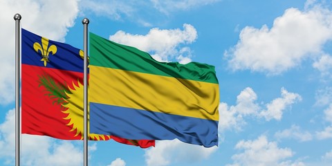 Guadeloupe and Gabon flag waving in the wind against white cloudy blue sky together. Diplomacy concept, international relations.