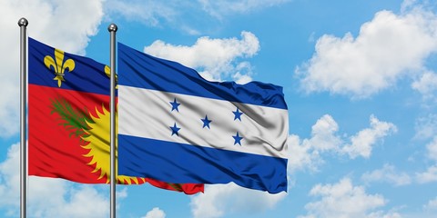 Guadeloupe and Honduras flag waving in the wind against white cloudy blue sky together. Diplomacy concept, international relations.