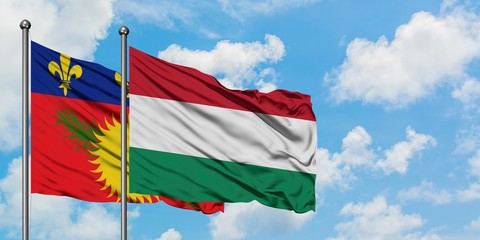 Guadeloupe and Hungary flag waving in the wind against white cloudy blue sky together. Diplomacy concept, international relations.