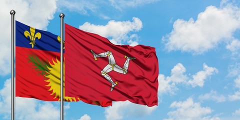 Guadeloupe and Isle Of Man flag waving in the wind against white cloudy blue sky together. Diplomacy concept, international relations.