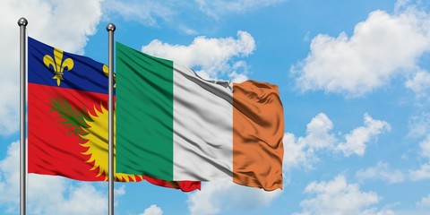 Guadeloupe and Ireland flag waving in the wind against white cloudy blue sky together. Diplomacy...