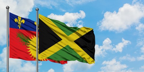 Guadeloupe and Jamaica flag waving in the wind against white cloudy blue sky together. Diplomacy...