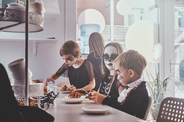Pretty kids in scary Halloween costumes have a festive party with tasty food and sweets.
