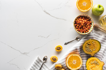 top view of striped towel with pumpkin, apricots, apple and orange near bowl with sea buckthorn on...