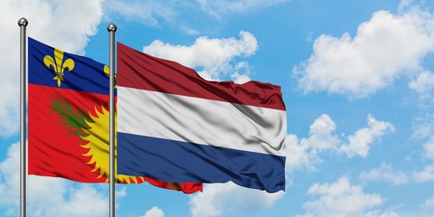 Guadeloupe and Netherlands flag waving in the wind against white cloudy blue sky together. Diplomacy concept, international relations.