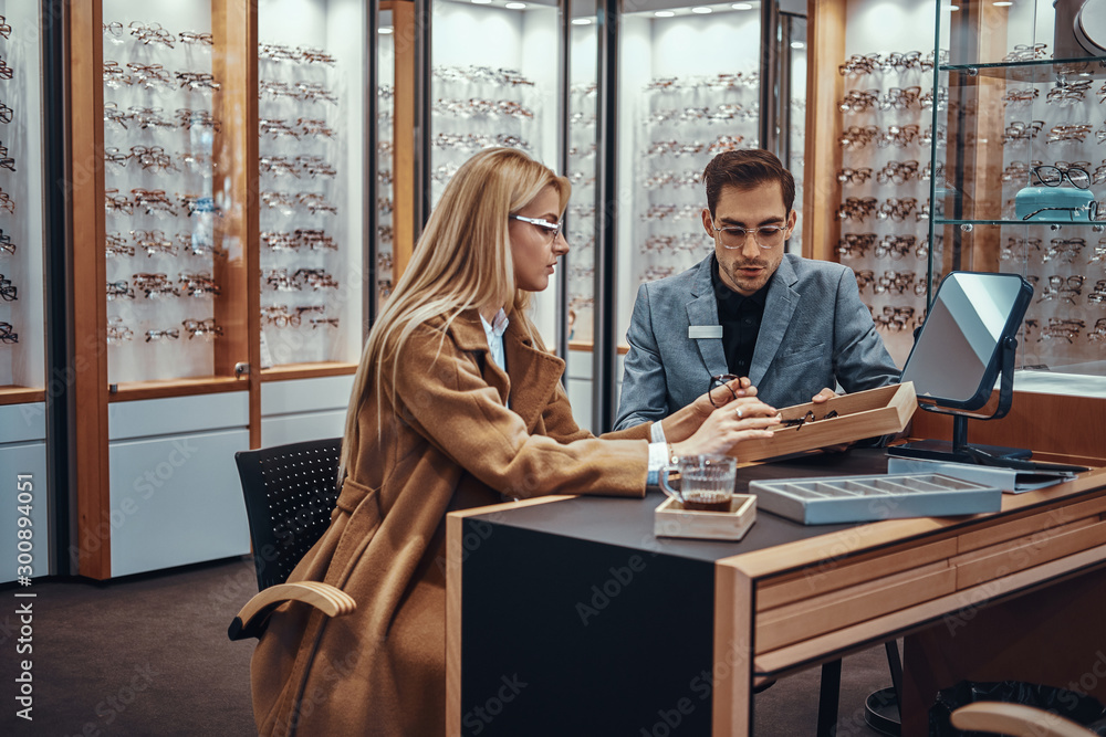 Wall mural professional salesperson helps a woman to choose reading glasses in an optometric shop.