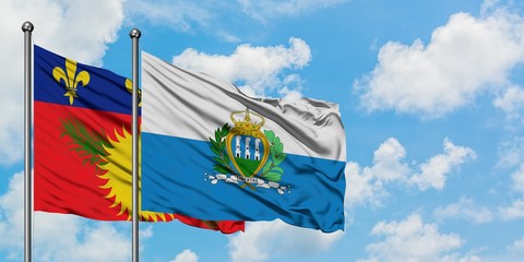 Guadeloupe and San Marino flag waving in the wind against white cloudy blue sky together. Diplomacy...