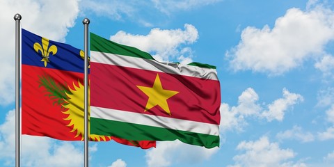 Guadeloupe and Suriname flag waving in the wind against white cloudy blue sky together. Diplomacy concept, international relations.