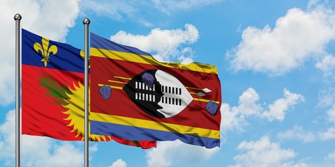Guadeloupe and Swaziland flag waving in the wind against white cloudy blue sky together. Diplomacy...