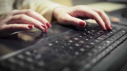 Close-up of woman's hands with red nails typing on a computer keyboard while sitting at office and working online